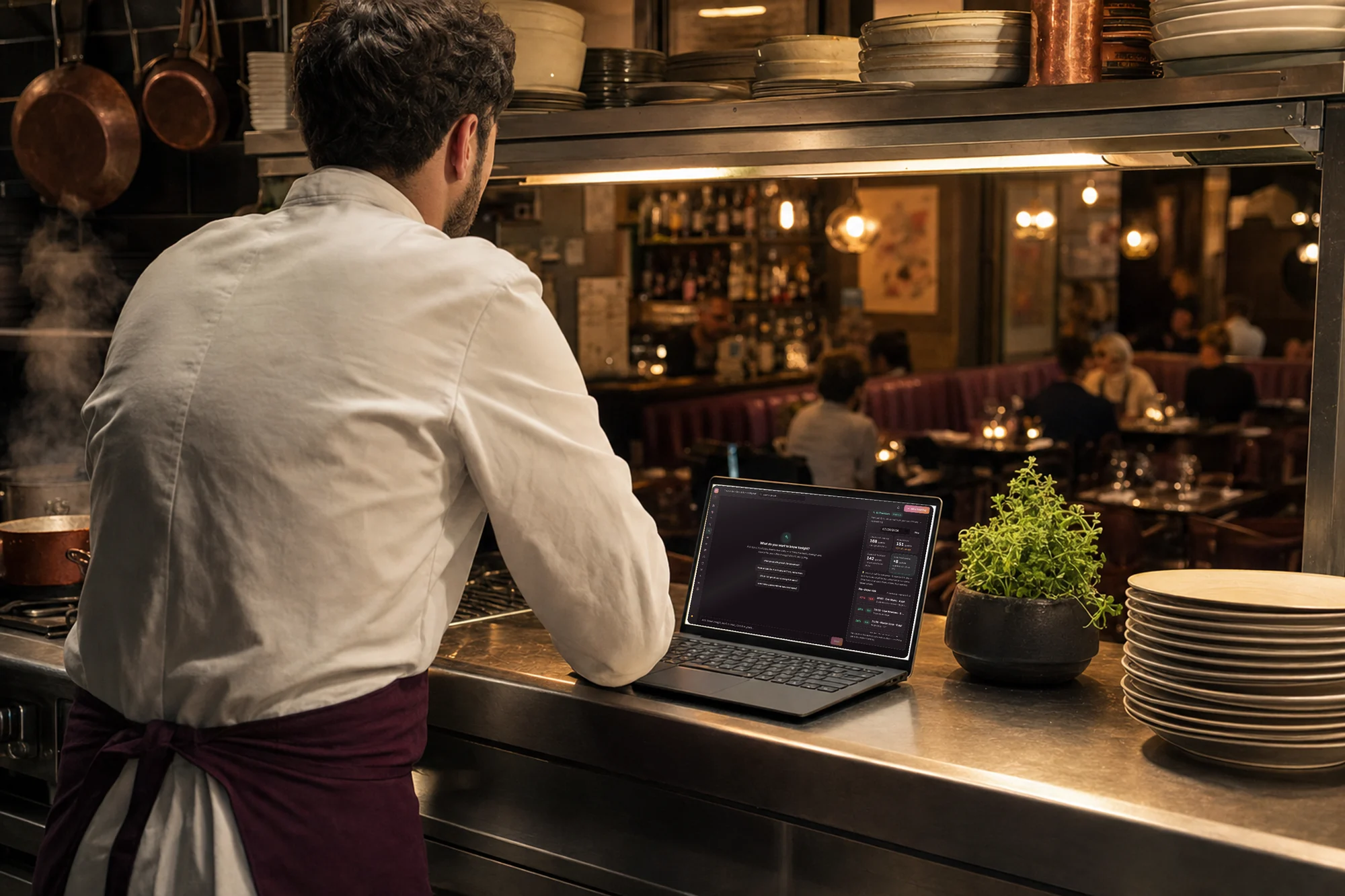 Chef at the kitchen pass with Goboblo AI on the laptop — the question How does tonight look? answered with tonight's bookings and no-show risk, the dining room behind