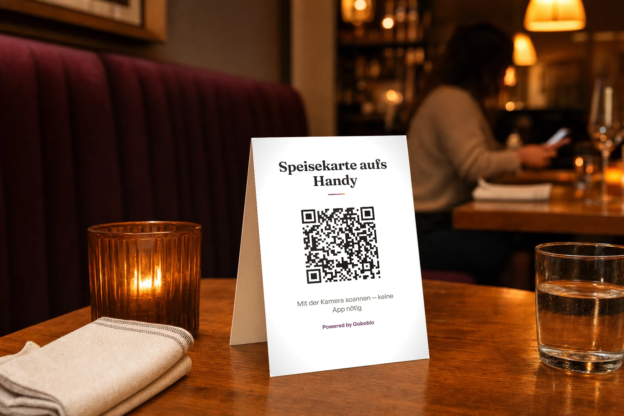 Tischaufsteller auf einem Restauranttisch mit deutschem Aufdruck „Speisekarte aufs Handy“ und einem echten QR-Code, der die Demo-Speisekarte öffnet – im warmen Abendlicht