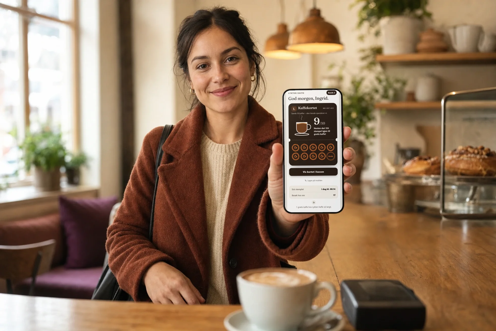 Gjest på en kafé holder opp mobilen mot kassen. Skjermen viser stempelkortet for kaffe med 9 av 10 stempler og teksten «Nesten der! Ett stempel igjen til gratis kaffe!»
